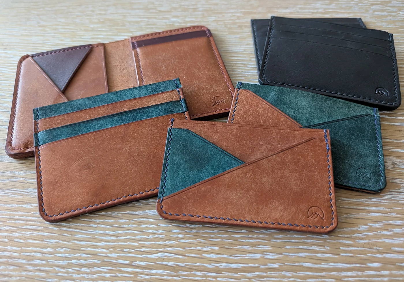 A collection of Moonlight Leatherworks wallets in black, brown, and green leather laid out together