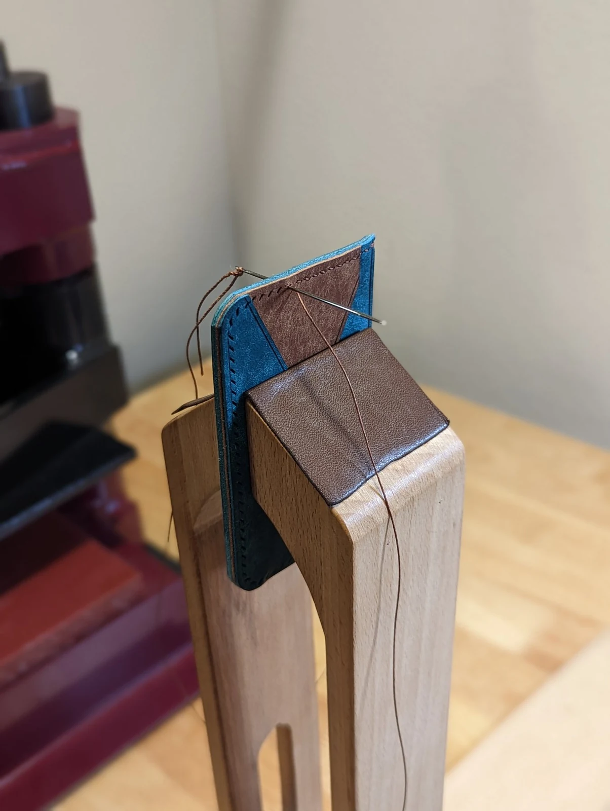 Close view of a wallet being saddle stitched by hand in a wooden stitching pony
